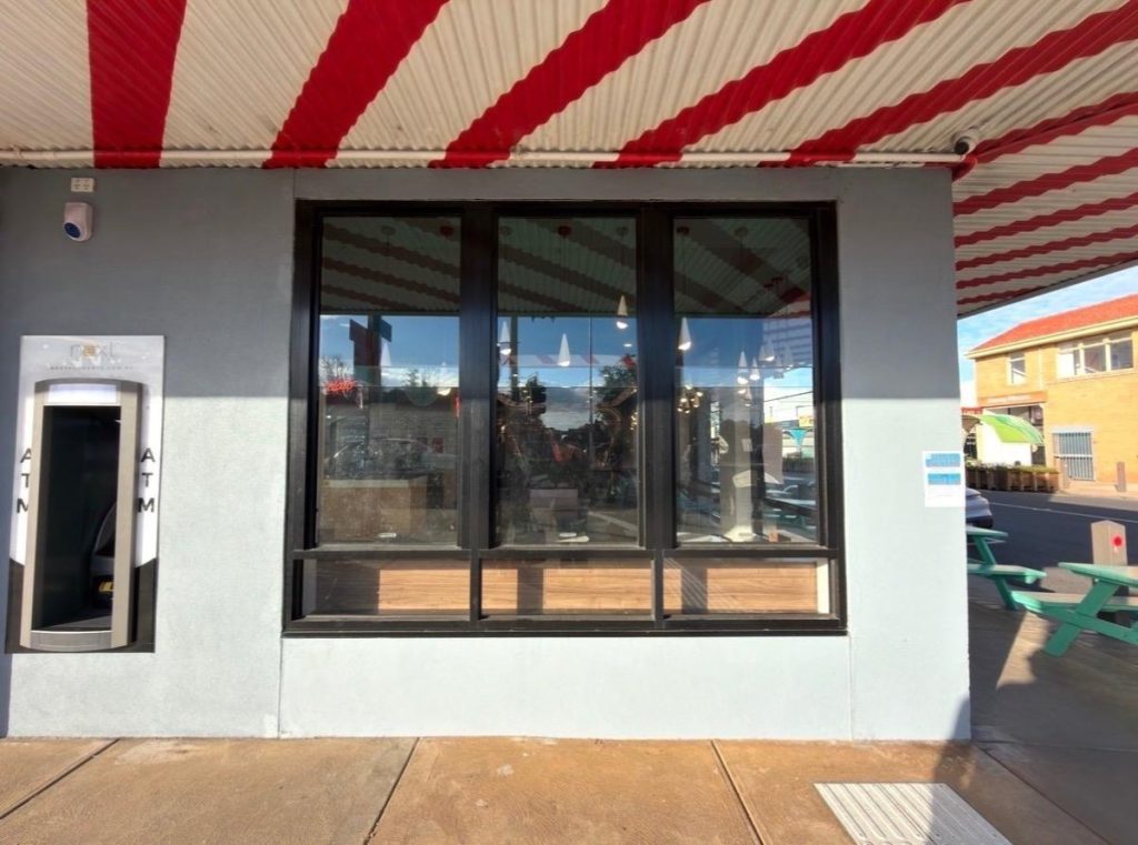 Storefront with a large black-framed window, an ATM on the left, and red-and-cream striped awning above.