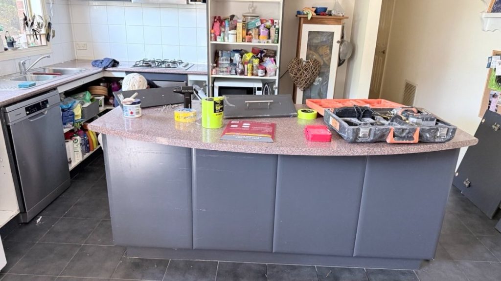 Kitchen with a large central island cluttered with tools, tape, a drill, and a toolbox, illustrating a DIY workspace in a home kitchen.