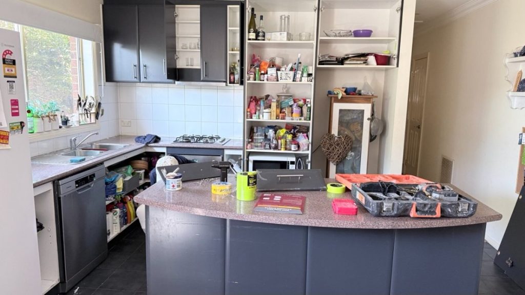 A messy kitchen with an island bench, open pantry shelves, and tools laid out on the counter.