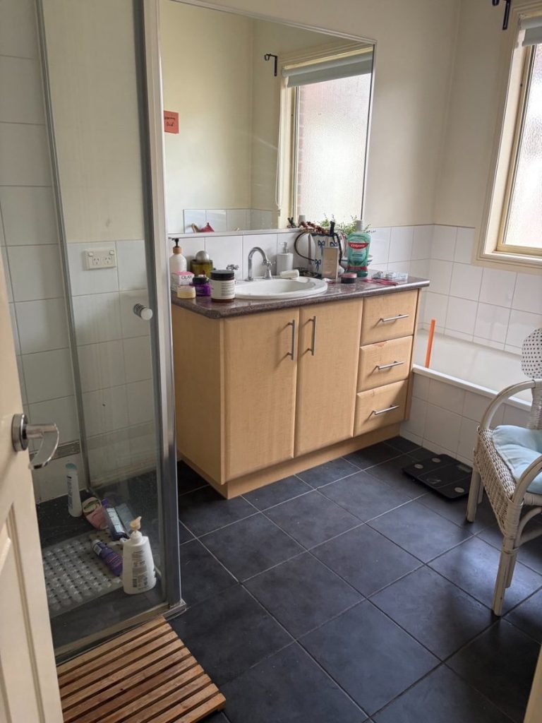 Bathroom with a wooden vanity, sink, and large mirror; shower on the left and a bathtub by a window.