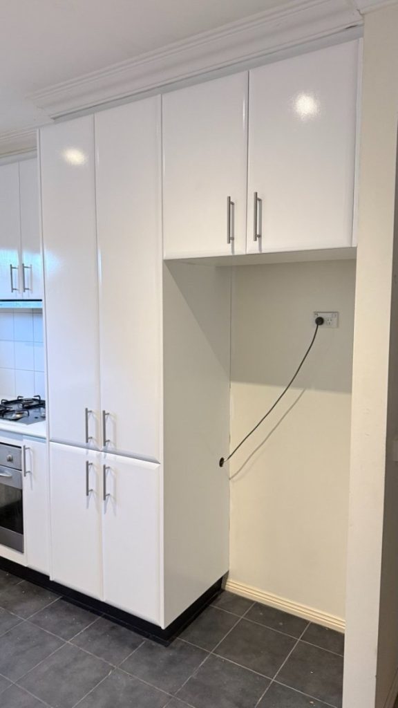 Tall white kitchen cabinetry with chrome handles, running along the wall, adjacent to an open alcove with an electrical outlet and loose cord inside.
