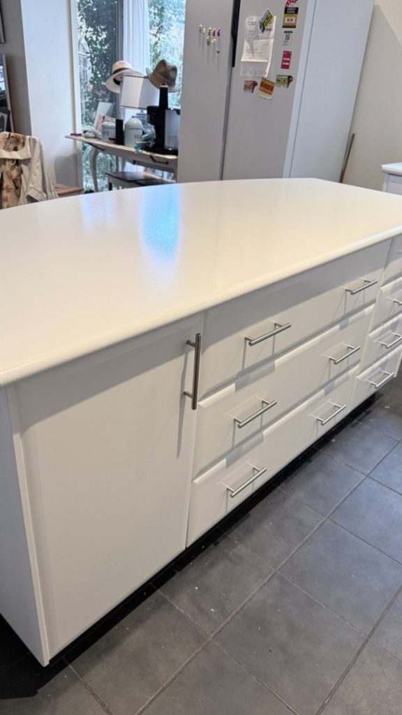 White kitchen island with multiple drawers and a glossy countertop in a bright, modern kitchen setting.
