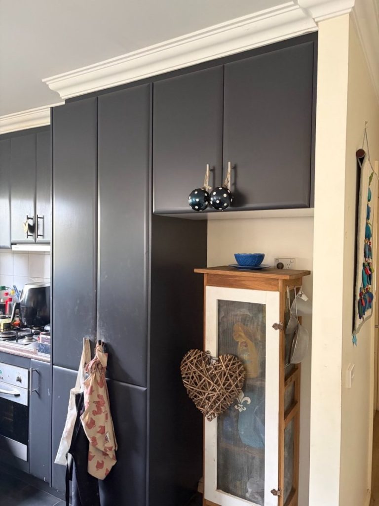 Tall dark gray kitchen cabinets line the wall, with a woven heart ornament hanging on a white-framed cabinet and a blue bowl on top nearby.
