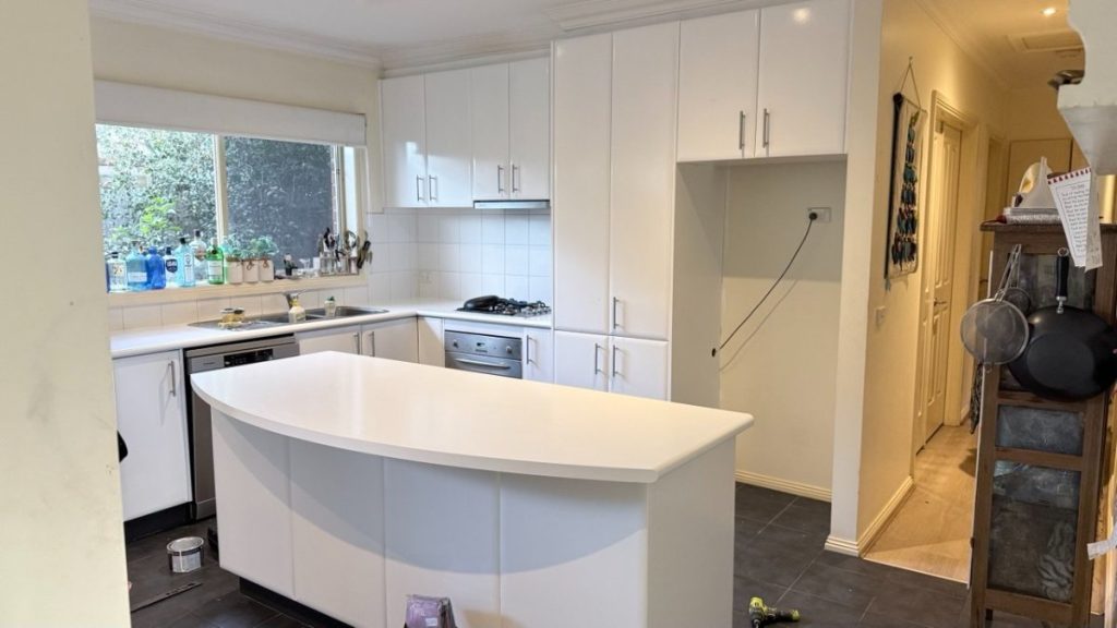 Bright all-white kitchen with a curved island, white cabinets, and a window above the sink.